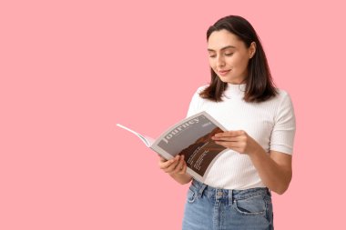 Güzel genç bayan pembe arka planda seyahat dergisi okuyor.