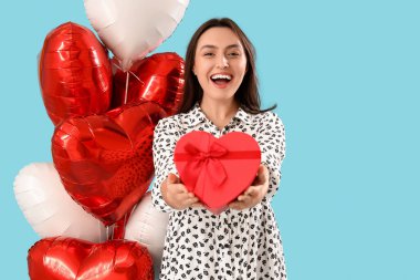 Mavi arka planda kalp şeklinde balonları olan genç bir kadın. Sevgililer Günü kutlaması