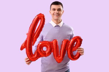 Leylak arka planında balonlardan yapılmış kelime aşkı olan genç bir adam. Sevgililer Günü kutlaması