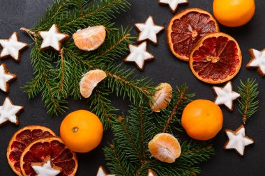 Yıldız şeklinde mandalinli zencefilli kurabiye, kurutulmuş portakal ve siyah arkaplanda köknar dalları