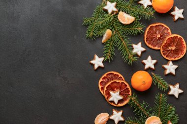 Yıldız şeklinde mandalinli zencefilli kurabiye, kurutulmuş portakal ve siyah arkaplanda köknar dalları