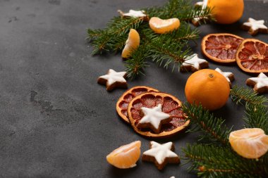 Yıldız şeklinde mandalinli zencefilli kurabiye, kurutulmuş portakal ve siyah arkaplanda köknar dalları
