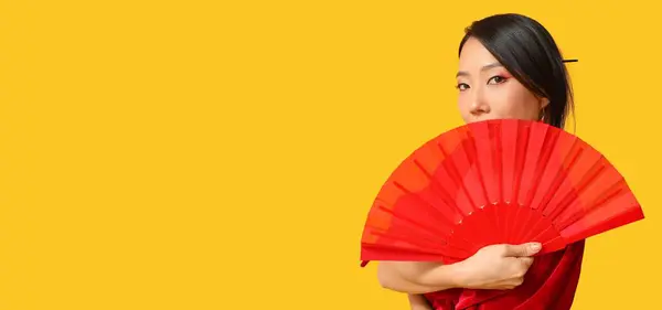 Beautiful Asian woman with fan on yellow background with space for text. Chinese New Year celebration
