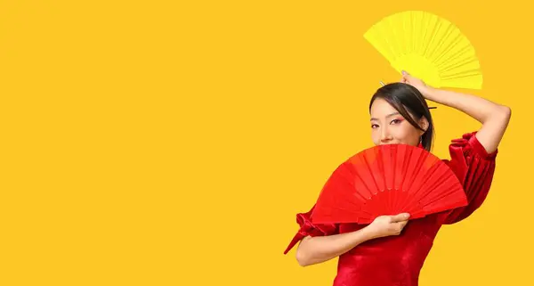 Beautiful Asian woman with fans on yellow background with space for text. Chinese New Year celebration
