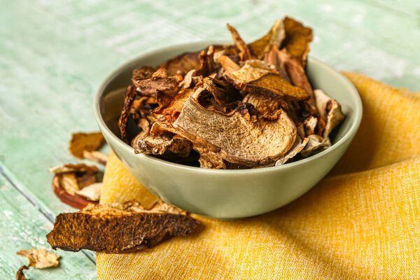 Bowl with tasty dried mushrooms on green wooden background