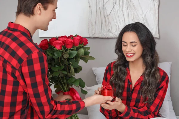 Young man with roses and ring proposing to his girlfriend in bedroom on Valentine\'s Day