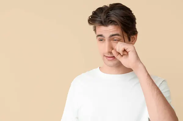 Young man with dry eyes on beige background. Glaucoma awareness month