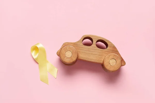 Golden ribbon with toy car on pink background. Childhood cancer awareness concept