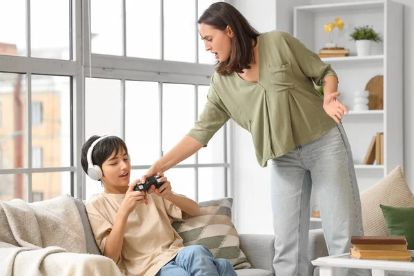 Angry mother taking game pad away from her teenage boy at home. Family problem concept