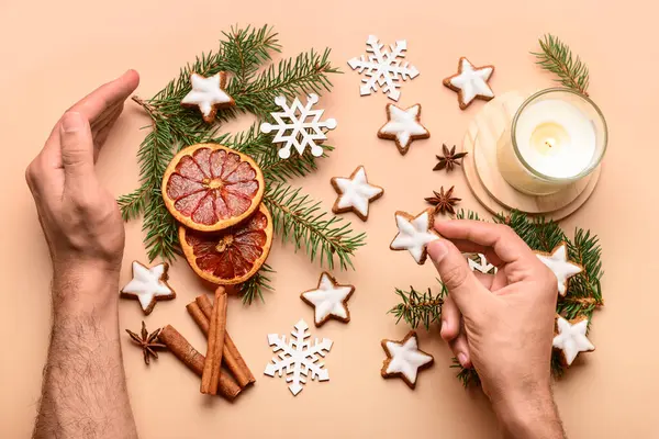 Male hands with star-shaped gingerbread cookies, cinnamon, dried orange, fir branches and burning candle on brown background
