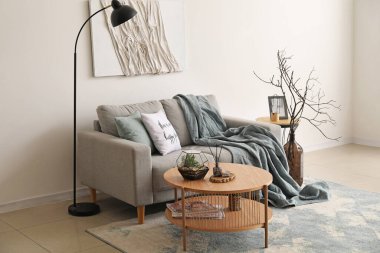 Beyaz duvarın yanında gri kanepesi ve kahve masası olan rahat bir oturma odası.