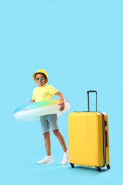 Mavi arka planda şişme yüzük ve bavulu olan küçük Afro-Amerikalı çocuk.