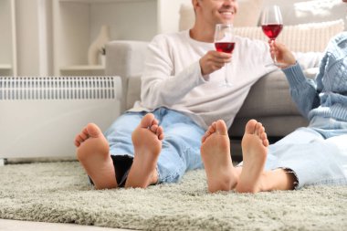 Evde kaloriferin yanında şarap ısıtan çıplak ayaklı genç bir çift.