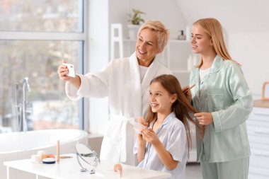 Annesi ve büyükannesiyle banyoda selfie çeken küçük bir kız.