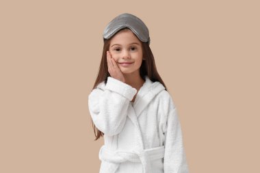 Bej arka planda uyku maskesi takan bornozlu tatlı küçük mutlu kız.