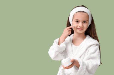 Yeşil arka planda krema kavanozu olan bornozlu tatlı küçük kız.