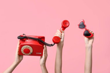 Klasik telefon ve pembe arka planda kalp şeklinde güneş gözlüğü tutan kadın eller. Sevgililer Günü kutlaması