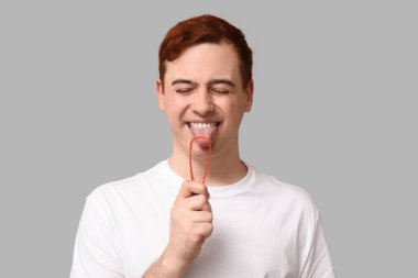 Gri arka planda dil kazıyıcısı olan genç bir adam.