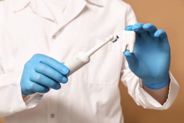 Bej arka planda elektrikli fırça ve diş modeline sahip dişçi, yakın plan. Dünya Diş Hekimi Günü