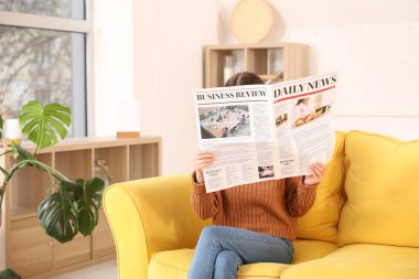 Young woman reading newspaper on sofa at home