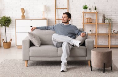 Oturma odasındaki kanepede oturan yakışıklı genç adam.