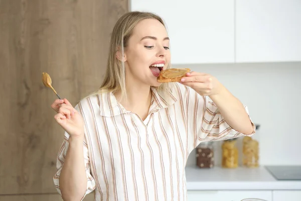 Young woman eating toast with nut butter in kitchen