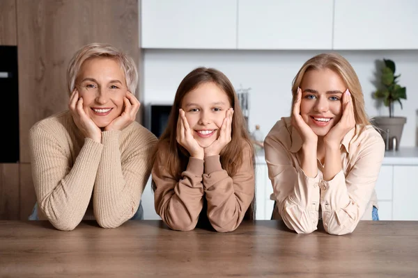 Little girl with her mom and grandmother smiling at table in kitchen