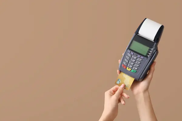 Woman with credit card and payment terminal on brown background