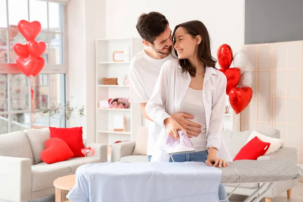 Happy young couple ironing shirt at home on Valentine\'s Day