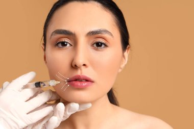 Genç bir kadın bej arka planda yüzlerine enjeksiyon yaptırıyor.