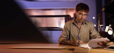 Geceleri ofiste çalışan dövmeli genç bir adam. Tasarım için pankart