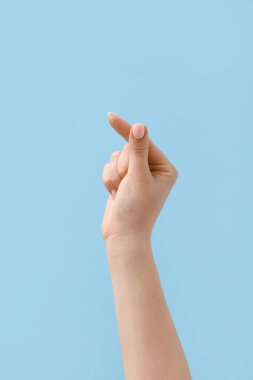 Mavi arka planda parmaklarıyla kalp yapan kadın.