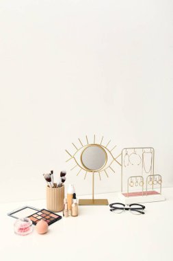 Farklı dekoratif kozmetik ürünler, beyaz masa üzerinde ayna ve mücevherler.