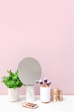 Odadaki pembe duvarın yanındaki tuvalet masasında farklı makyaj malzemeleri, ayna ve bitkiler var.
