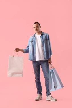 Pembe arka planda alışveriş torbaları olan genç adam.