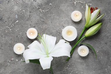 Güzel zambak çiçekleri ve gri arka planda yanan mumlar