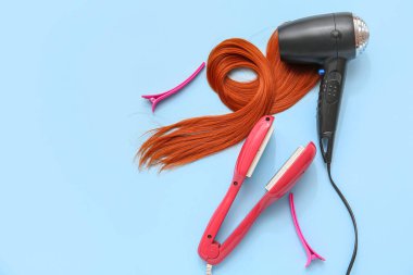Saç kurutma makinesi, iplik, düzleştirme demiri ve açık mavi arka planda klipsler.