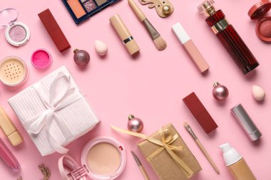 Farklı makyaj ürünlerinden yapılmış çerçeve ve pembe arka planda Noel topları