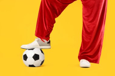 Sarı arka planda futbol topu olan sportif Noel Baba, yakın plan.