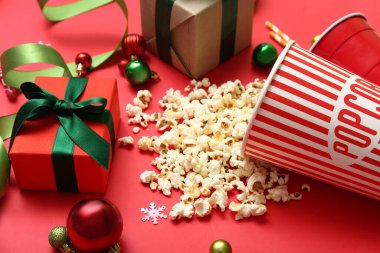Bir kova patlamış mısır, hediyeler ve kırmızı arka planda Noel süsü.