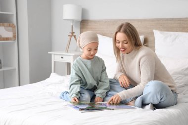 Annesi yatak odasında kitap okurken kemoterapiden sonra küçük bir Asyalı kız.