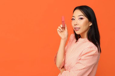 Turuncu arka planda sıvı ruj olan güzel bir Asyalı kadın.