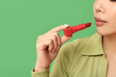 Yeşil arka plana ruj süren güzel Asyalı kadın, yakın plan.