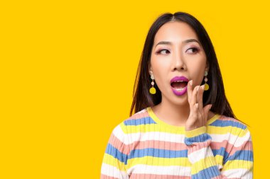 Sarı arka planda mor ruj sürmüş güzel, şaşırmış Asyalı kadın.