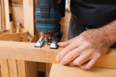 Olgun marangoz, atölyedeki masada yapboz testeresiyle tahta testeresi kesiyor.