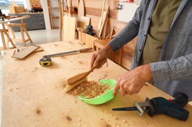 Olgun marangoz dükkandaki masaları süpürüyor, yakın plan.