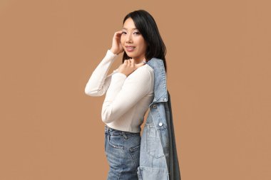 Kahverengi arka planda şık kot elbiseli güzel, mutlu bir Asyalı kadın.