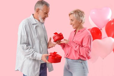 Olgun çift pembe arka planda hediyelerle birbirlerini selamlıyorlar. Sevgililer Günü kutlaması