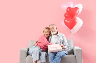 Kanepede pembe arka planda hediyelerle kucaklaşan olgun bir çift. Sevgililer Günü kutlaması