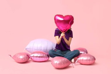 Pembe arka planda kalp şeklinde balonları olan genç bir kadın. Sevgililer Günü kutlaması